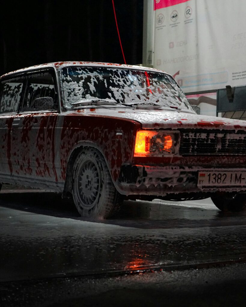 A classic vintage car covered in soap foam at a carwash during nighttime.