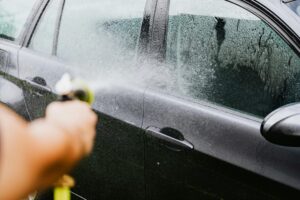 A car being washed with a hose outdoors. Water sprays create a cleaning effect on the vehicle.